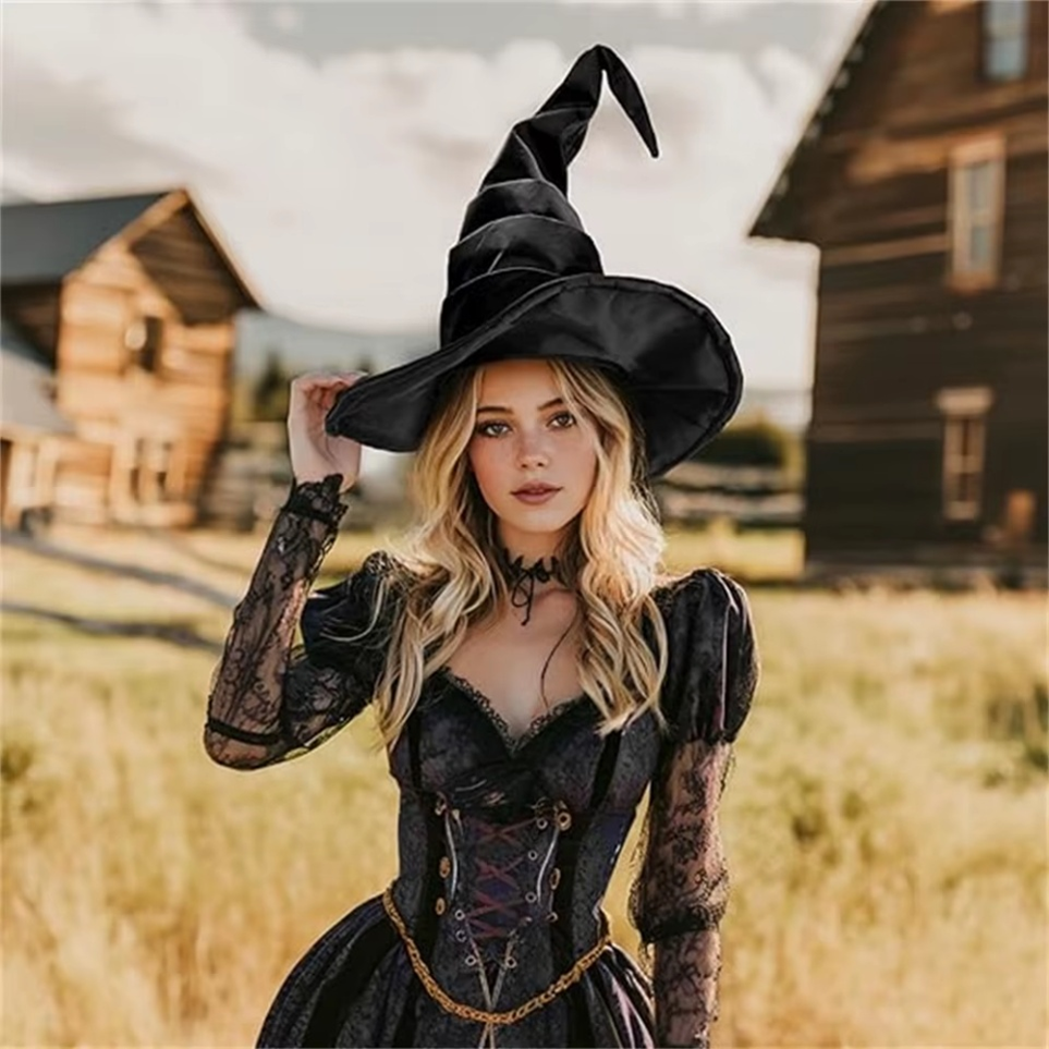 Woman in a witch costume with a large black hat in a rustic outdoor setting.