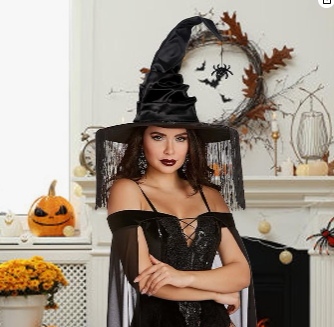 Woman in a black witch costume with a large witch hat in a Halloween-themed room.