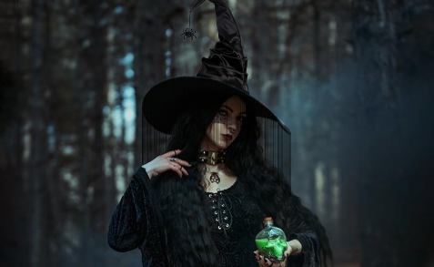 Woman in a dark witch costume holding a green potion bottle in a forest setting